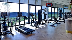 Un gimnasio moderno con diversos equipos de ejercicio, ventanas amplias y suelo de madera en diseño de espiga.