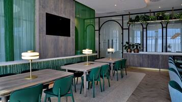 A modern restaurant interior with green chairs, wooden tables, and a green textured wall.