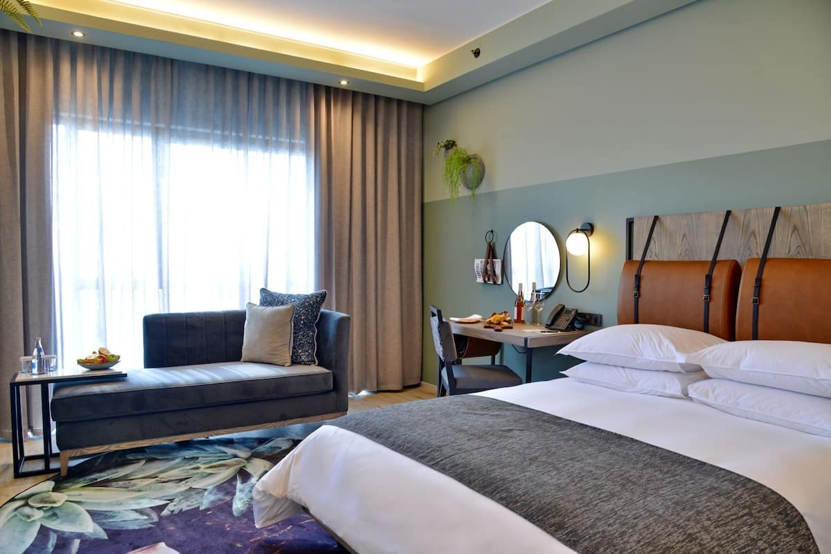 A hotel room with a bed, a sofa, a desk, and a large window with curtains.