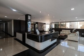 A modern hotel lobby with a reception desk, a seating area with sofas, and a large window providing natural light. - Hotel Havana Express (Uberaba)