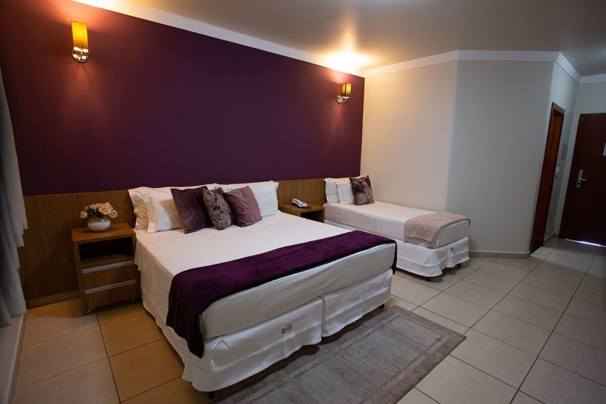 A hotel room with a large bed, a smaller bed, a nightstand, a lamp, and a door.