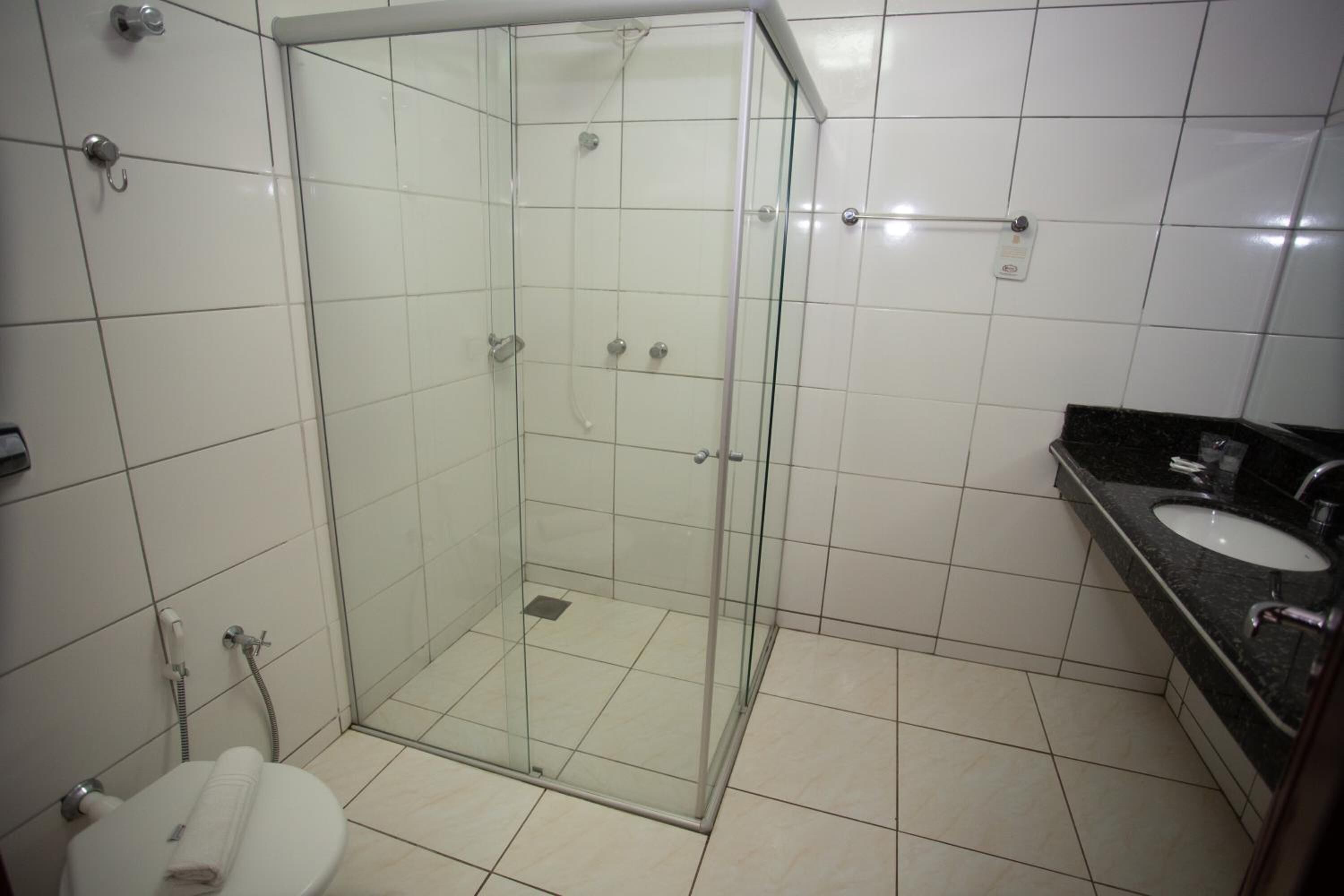 Un baño con ducha envuelta en vidrio, un inodoro y un lavamanos con encimera negra.