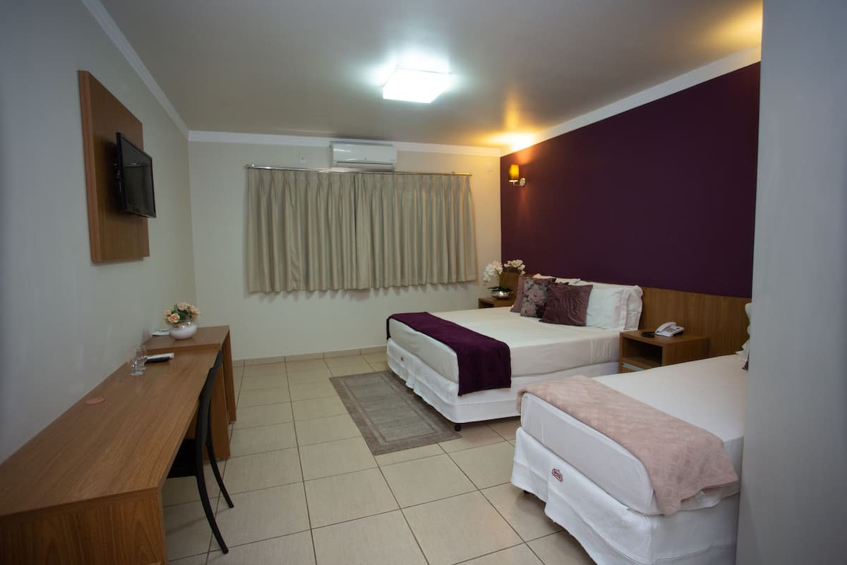 A hotel room with two beds, a desk, a TV mounted on the wall, and an air conditioning unit.
