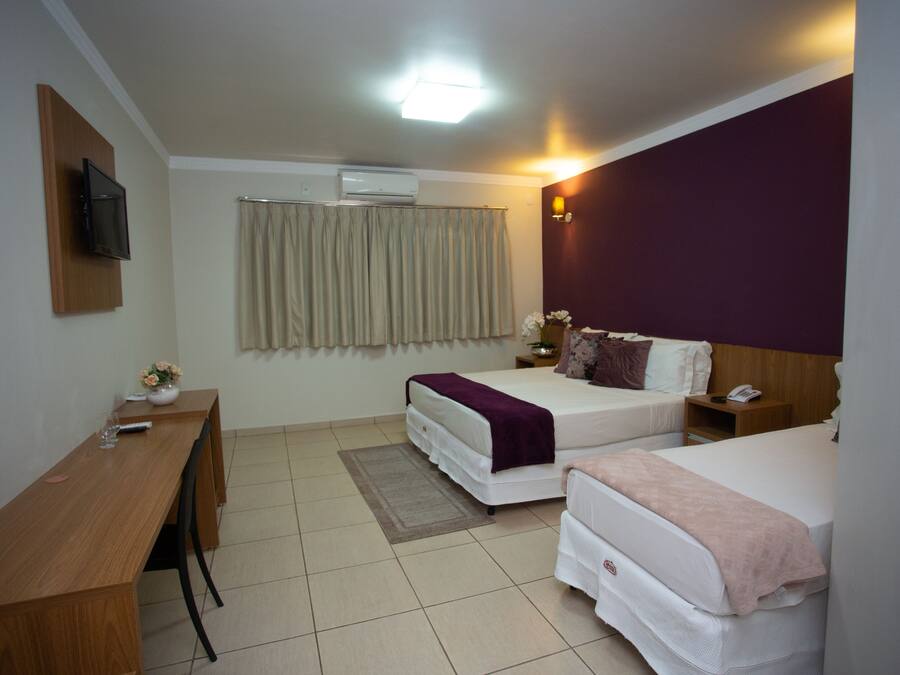 Een hotelkamer met twee bedden, een bureau, een aan de muur bevestigde televisie en een airconditioning.