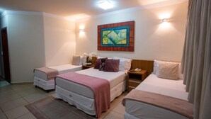 Habitación de hotel con dos camas individuales, una cama grande, un cuadro en la pared y una mesita de noche con lámpara.