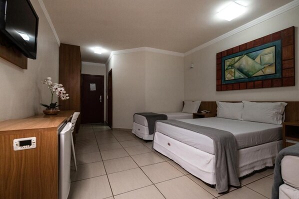 A hotel room with a bed, bedside table, TV, and a painting on the wall.