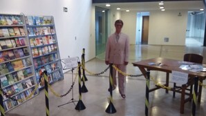 Una persona de pie en un pasillo con una mesa y sillas, rodeada de estanterías.