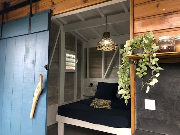 Un dormitorio con cama, una planta colgante, estante con frascos y una lámpara de diseño único.