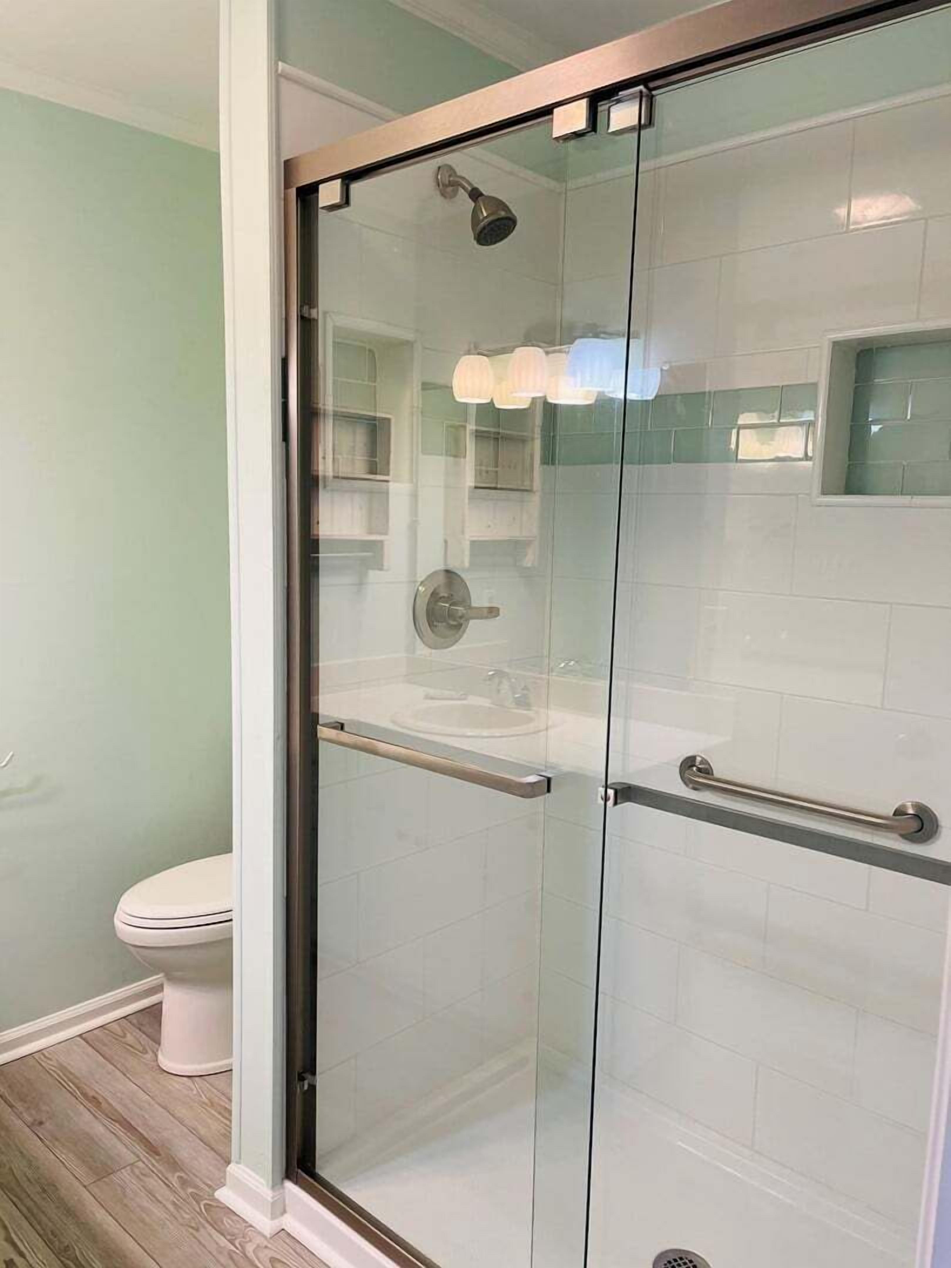 A glass-enclosed shower with a handheld showerhead, a handheld showerhead, and a handheld showerhead.