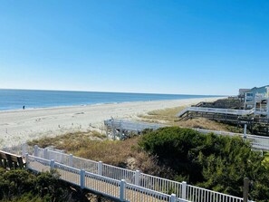 Blick auf einen Strand mit einer Holzpromenade, die zu einem mehrstöckigen Gebäude mit Balkonen führt.