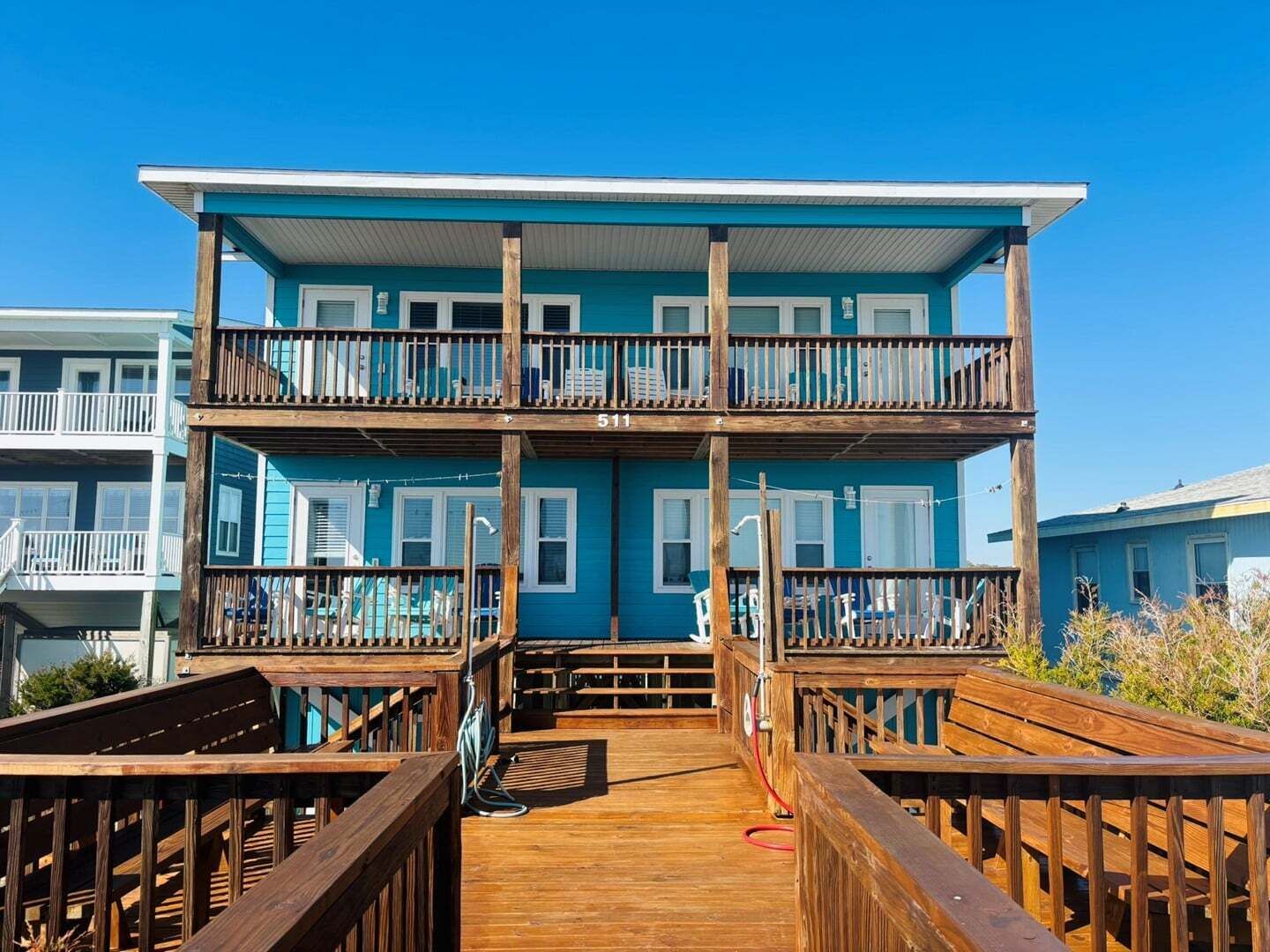 Un bâtiment à deux étages, doté d’un balcon à chaque niveau, d’une terrasse en bois à l’avant et surplombant un ciel d’un bleu éclatant.