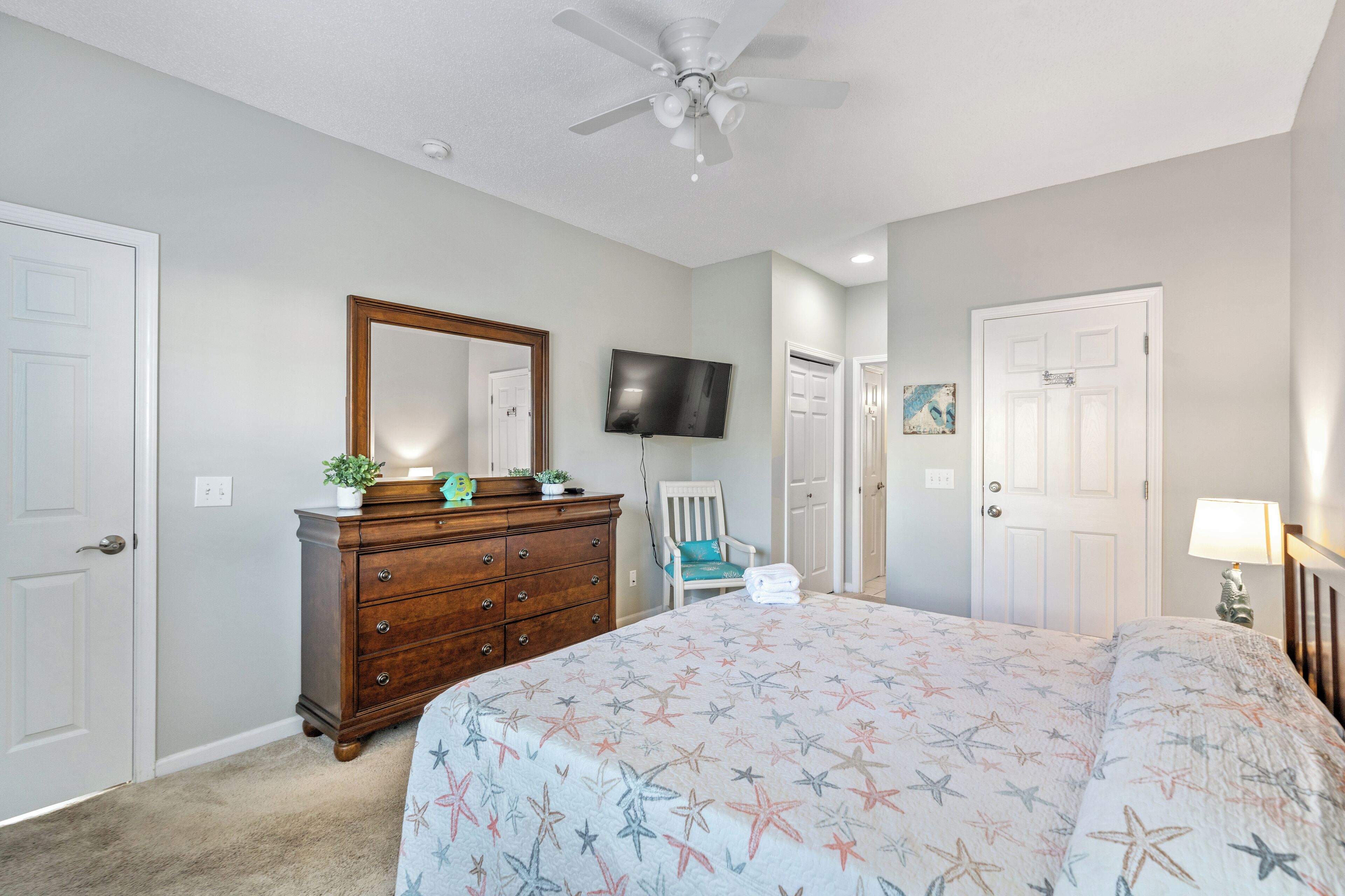 A bedroom with a bed, dresser, TV, chair, and ceiling fan.