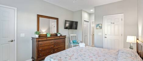 A bedroom with a bed, dresser, TV, chair, and ceiling fan.