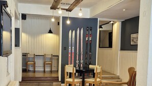 A spacious room with a wooden floor, a dining table with chairs, a wall-mounted ski rack, and a staircase leading to another level. - Hotel Nordico (San Carlos de Bariloche)