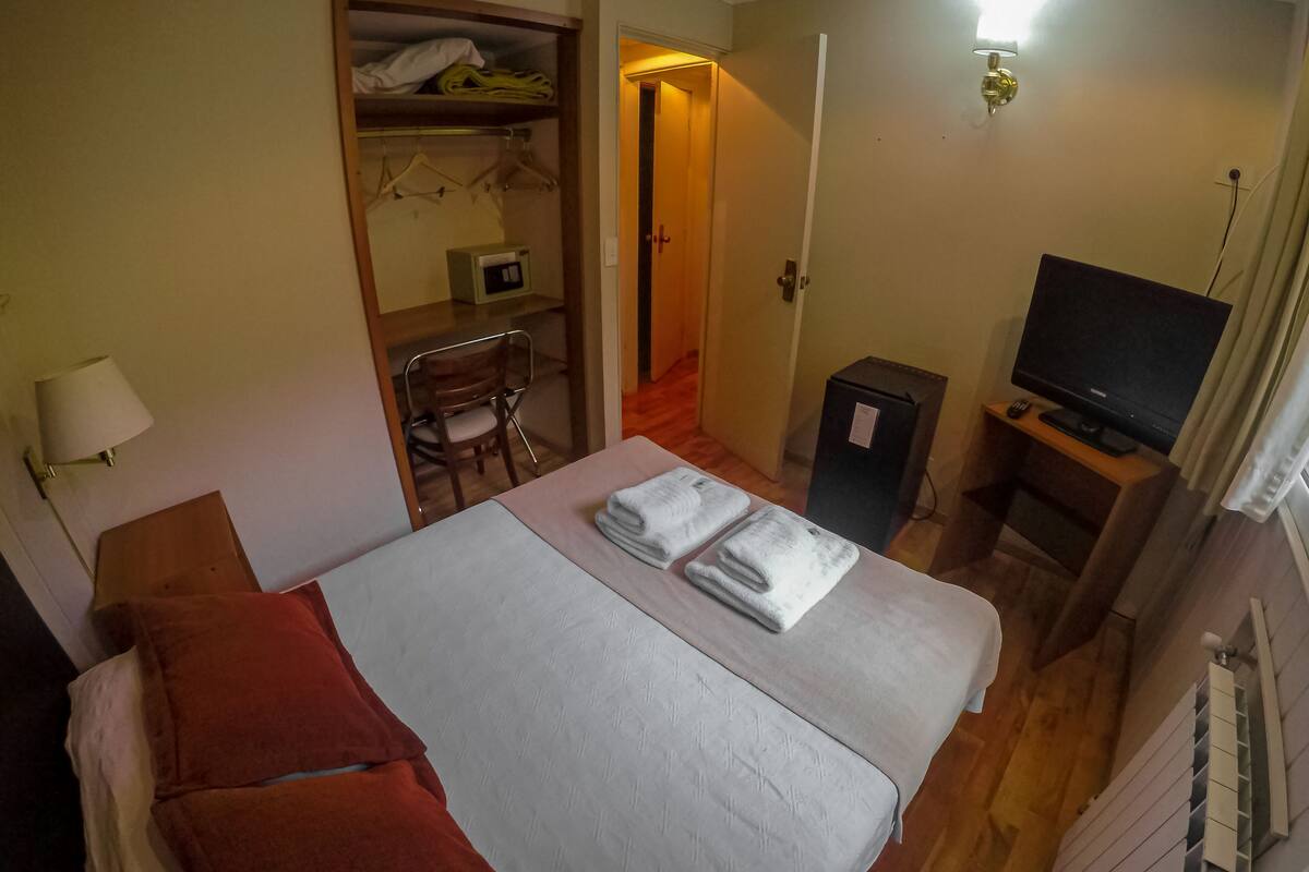 Habitación de hotel con cama, escritorio, silla, televisor y armario.