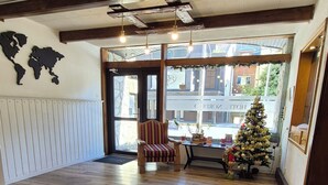 A spacious room with wooden flooring, a striped chair, a small Christmas tree, and a world map on the wall. - Hotel Nordico (San Carlos de Bariloche)