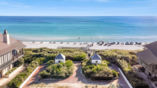 Une vue sur la plage, avec un sentier menant à deux petites constructions blanches, surplombant une plage très fréquentée.