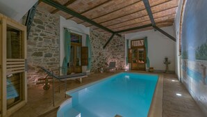 A swimming pool with stone walls and wooden beams, surrounded by stone flooring and a bench.