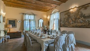 A dining room with a long table set for a meal, featuring a rustic brick ceiling and a large landscape painting on the wall.
