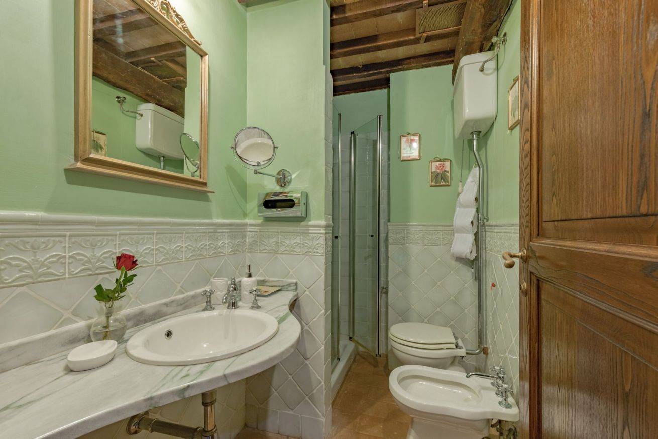 Een badkamer met een marmeren wastafel, een douchecabine van glas en een houten deur.