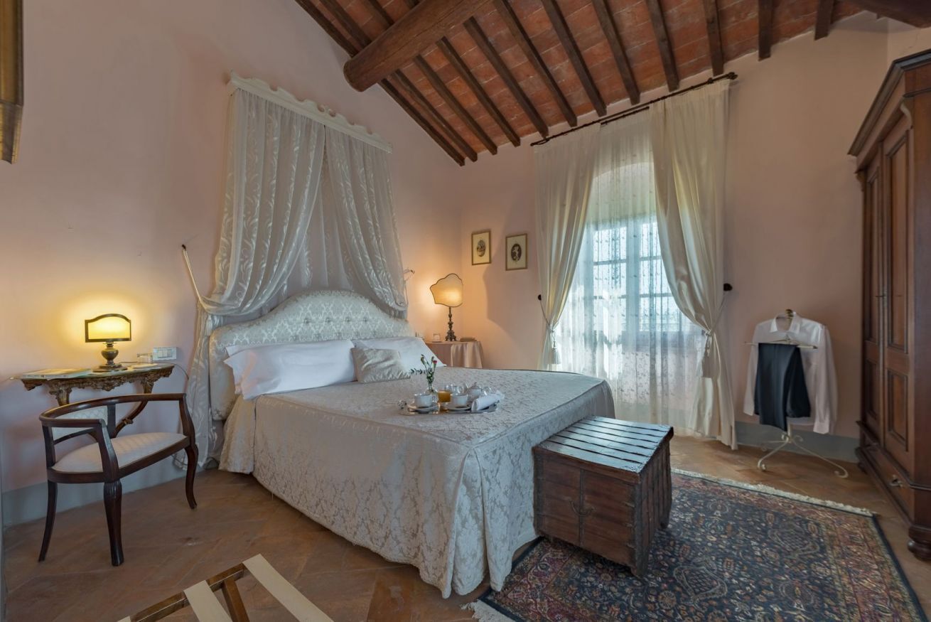 Een slaapkamer met een groot bed, een nachtkastje met een lamp, een houten bankje en een kledingkast.