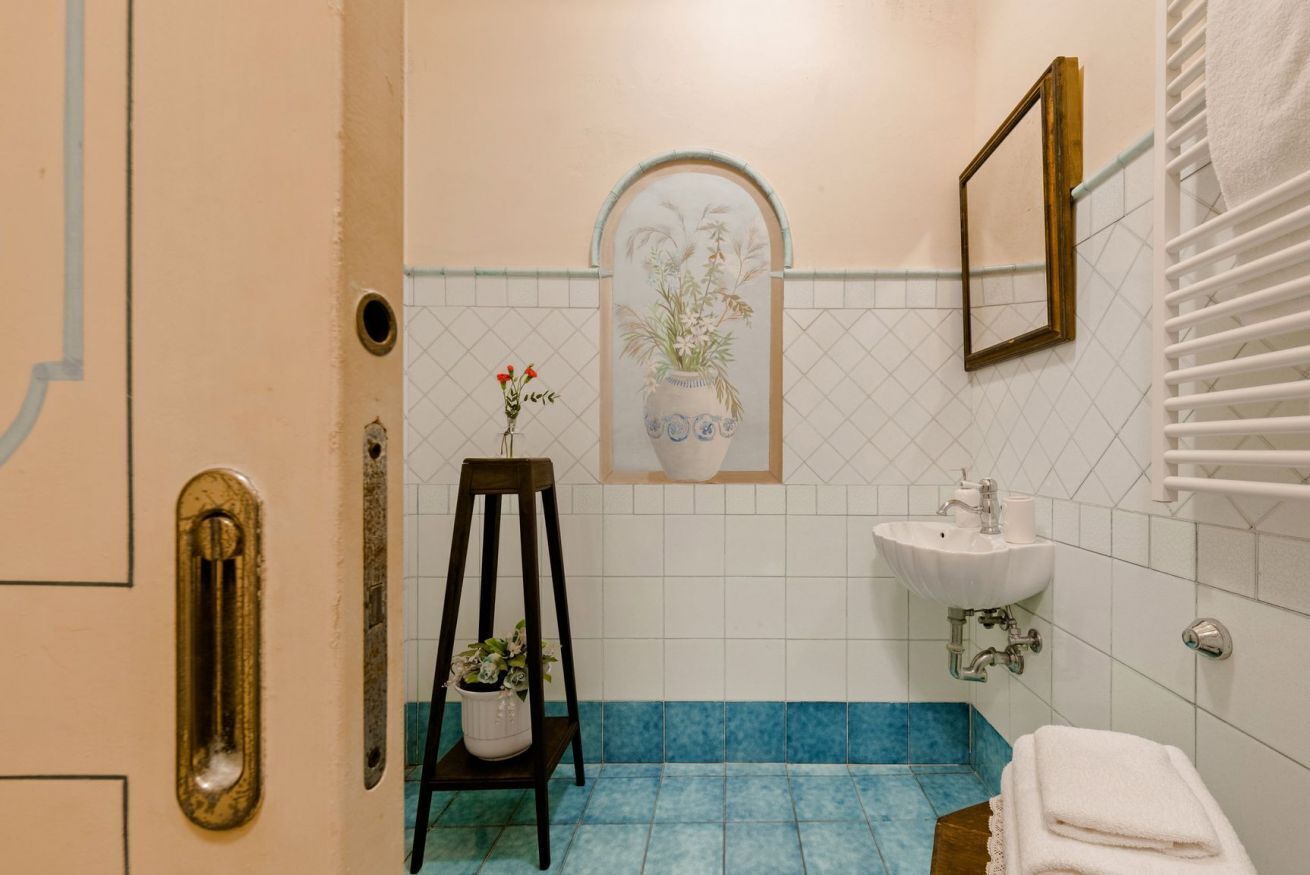 Une salle de bain avec un lavabo, un miroir et une plante décorative posée sur une chaise.