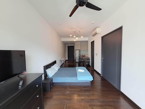 Ein modernes Schlafzimmer mit einem großen Bett, einem Fernseher, einem Deckenventilator und einer Küchenzeile im Hintergrund.