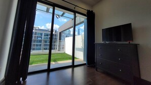 Una habitación moderna con puerta de vidrio corredera que da a un balcón, un televisor de pantalla plana sobre una cómoda y un diseño limpio y minimalista.