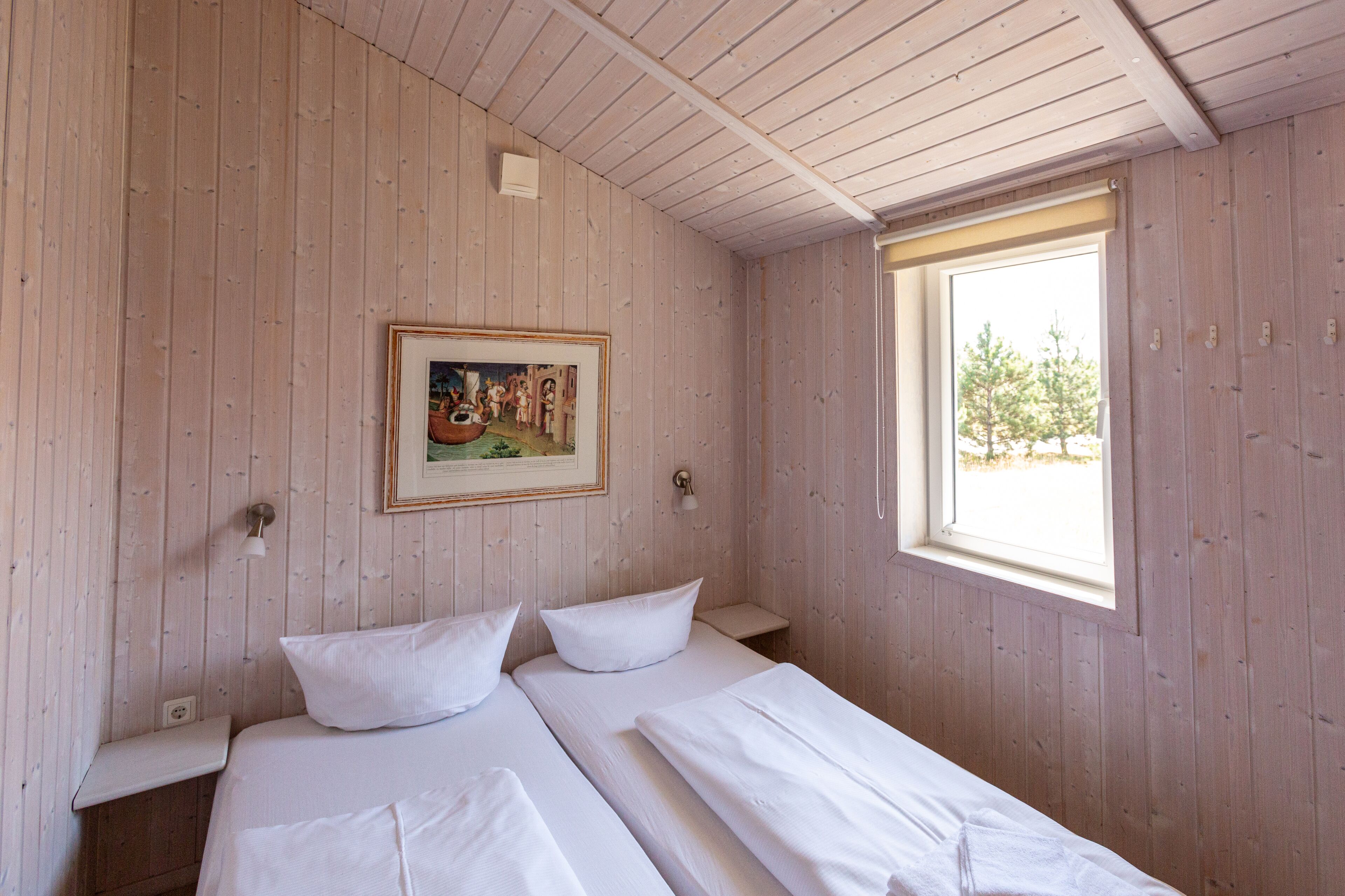 Ein Zimmer mit zwei Betten, Holzwänden, einem Fenster und einem gerahmten Bild an der Wand.