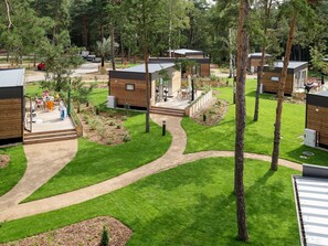 A modern outdoor area with wooden cabins, a paved walkway, and a grassy lawn.