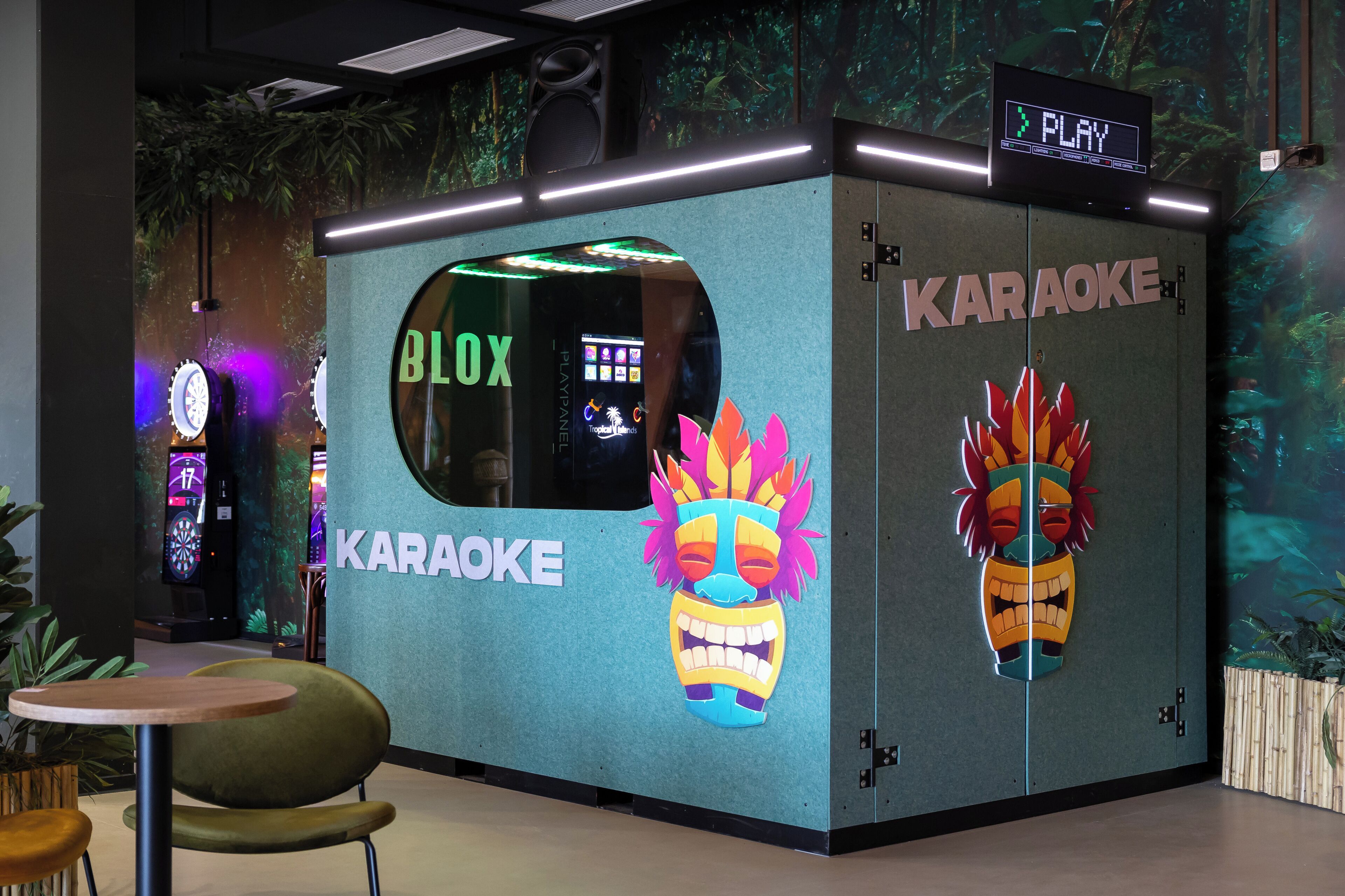 Cabine de karaokê com tela digital exibindo 'PLAY' e 'KAROKE'.