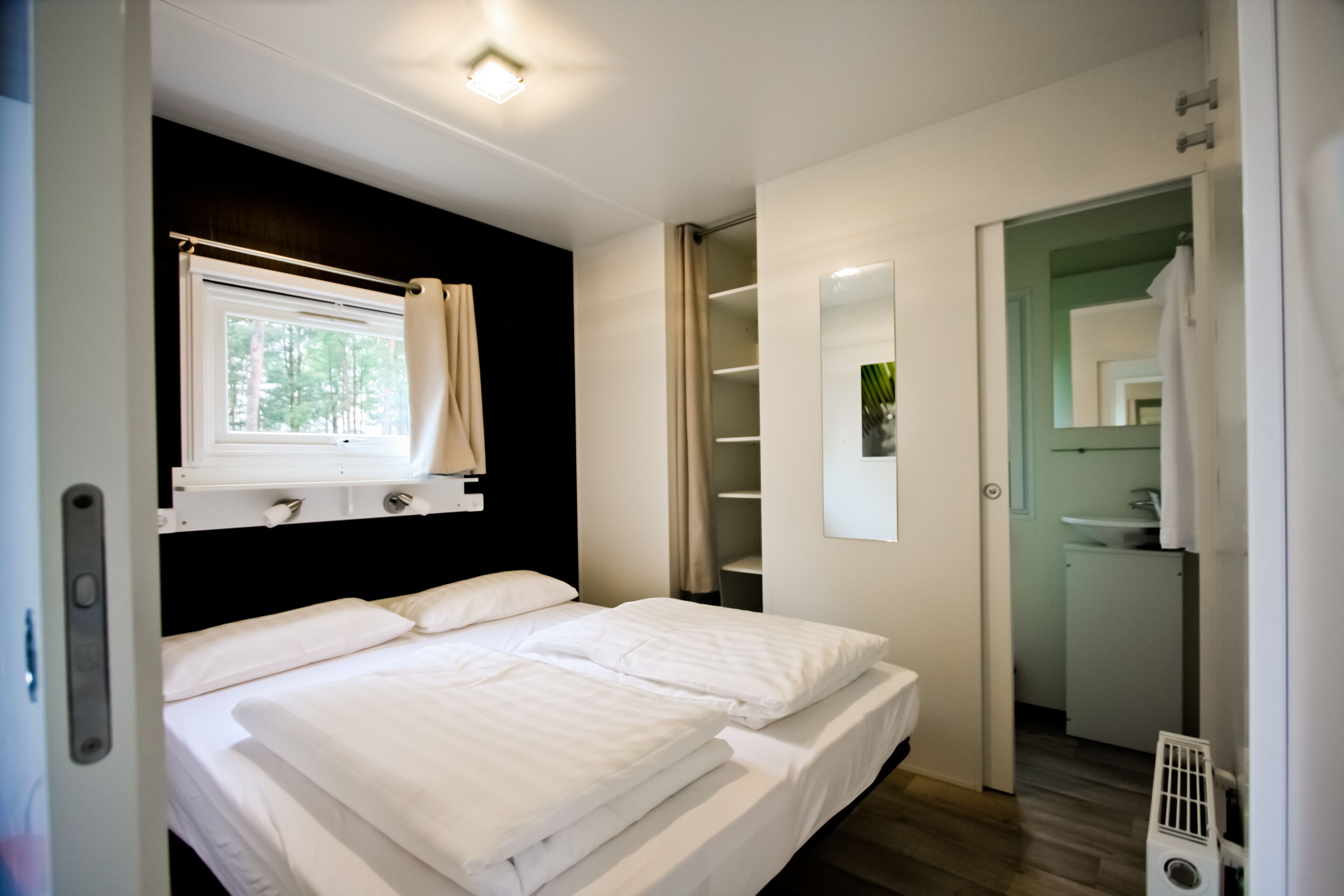 A bedroom with two beds, a window with curtains, a mirror, and a walk-in closet.