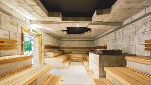 Una sauna con bancos de madera, un muro de piedra y una zona central con bancos.