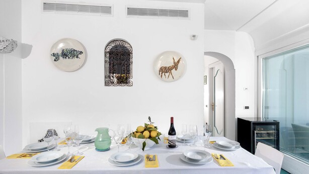 A dining area with a white table set for a meal, decorated with a vase of lemons and a bottle of wine. - Villa Le Sirene with Private Jacuzzi, Sea View (Positano)