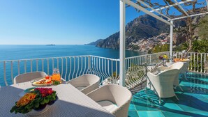 A terrace with wicker furniture, a table with a fruit plate and drinks, and a view of the sea and mountains. - Villa Le Sirene with Private Jacuzzi, Sea View (Positano)