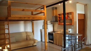 Una habitación acogedora con una cama litera, un sofá, una zona de cocina y una mesa de comedor.