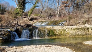 Un paisaje natural con una cascada pequeña, terreno rocoso y árboles.