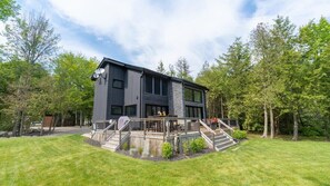 A modern two-story house with a deck and stairs leading to a covered outdoor seating area.