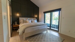 A bedroom with a large bed, a nightstand, a wall-mounted light, and a view through a sliding glass door.