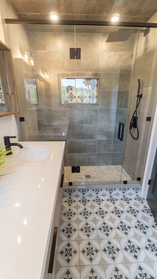 Un baño moderno con ducha envuelta en vidrio, un lavabo blanco y baldosas de suelo estampadas.