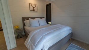 Un dormitorio con cama, mesita de noche, un cuadro en la pared y una puerta.