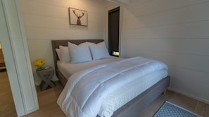 Un dormitorio con cama, mesita de noche, un cuadro en la pared y una puerta.