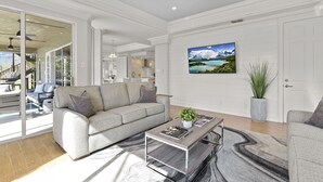 Uma sala de estar moderna com um sofá cinzento, uma mesa de centro e uma televisão grande fixada na parede.