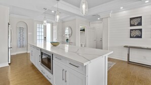 Cozinha moderna com armários brancos, uma ilha grande, iluminação pendente e vista para a sala de jantar.