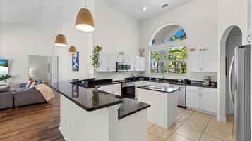 Une cuisine moderne avec des meubles blancs, un îlot central et des luminaires suspendus.