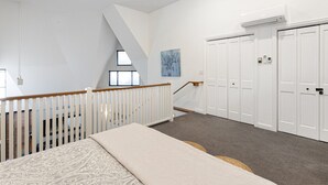Ein Schlafzimmer mit schrägverdeckter Decke, einem Bett, einer Treppe und mehreren weißen Schränken.