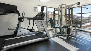 Ein Fitnessstudio mit Laufband, Kraftgeräten und einem Fernsehbildschirm.