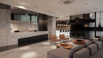 Un hall d'entrée moderne avec un comptoir d'accueil, un espace salon et une cuisine en arrière-plan.