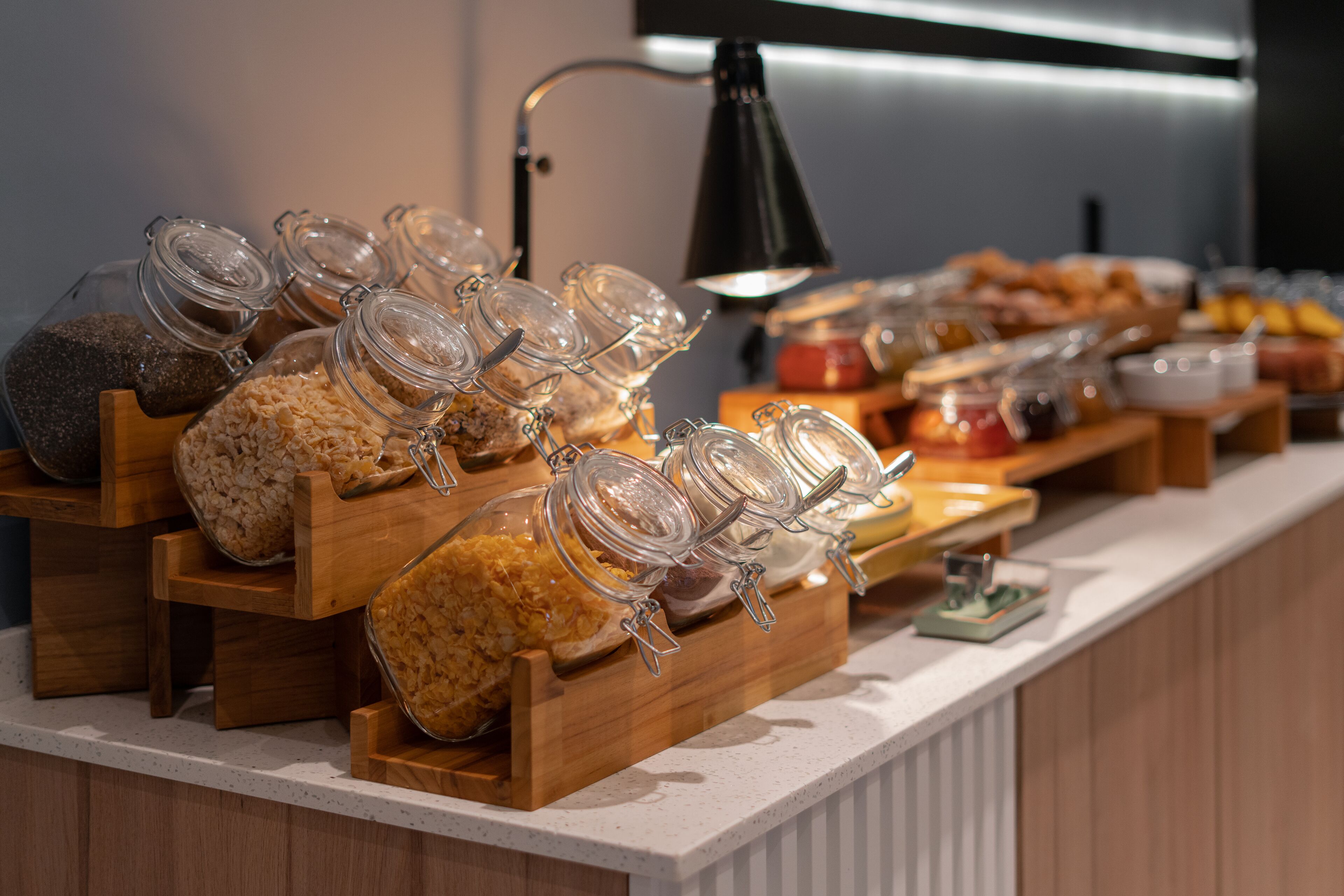 Buffet com diversos alimentos em potes e recipientes de vidro, dispostos sobre suportes de madeira.