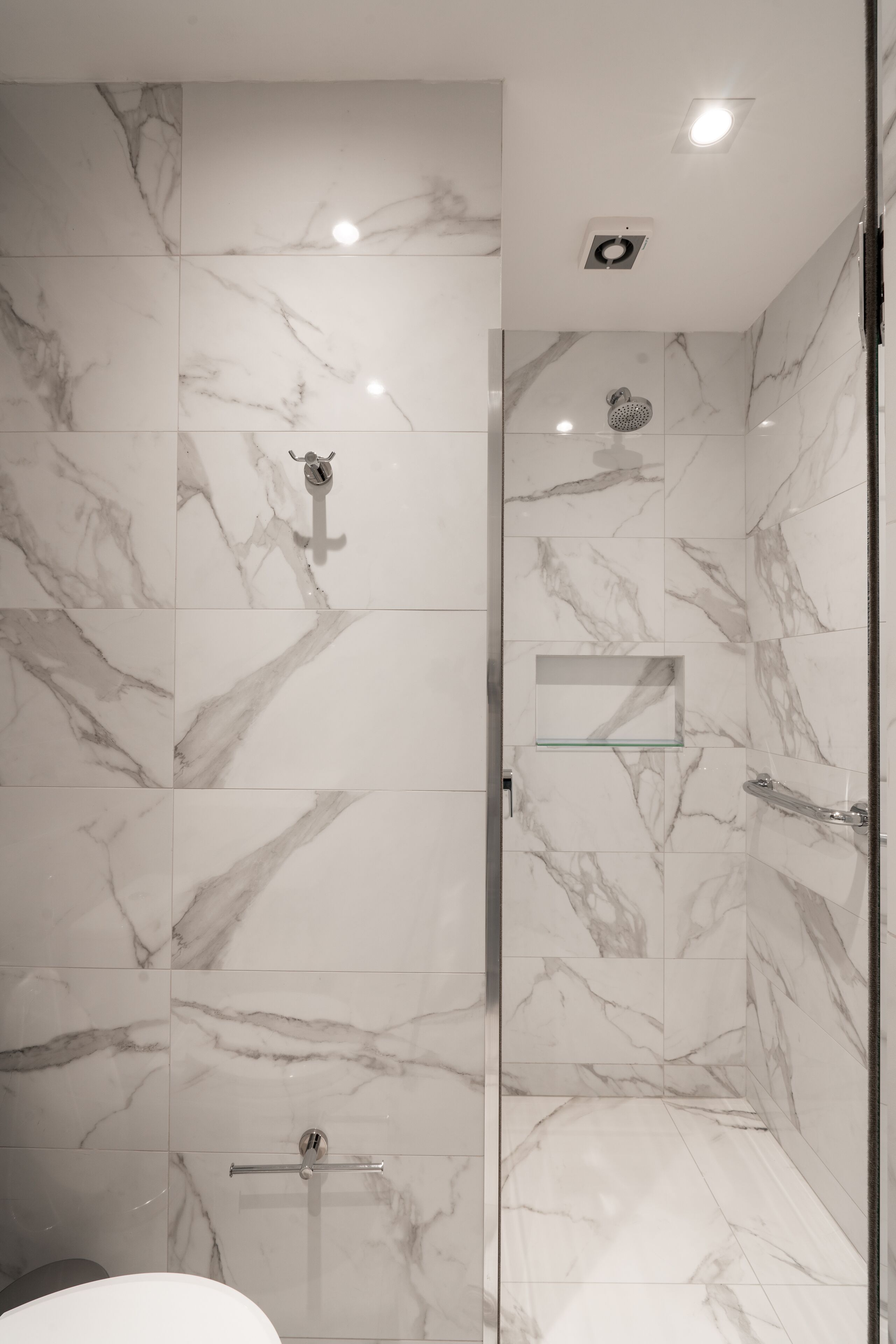 A modern bathroom with marble tiles, a glass shower enclosure, and a visible toilet.